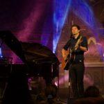Portrait des Künstlers Lennert Schilgen mit Gitarre in bunt beleuchteter Kirche