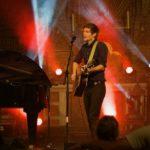 Portrait des Künstlers Lennert Schilgen mit Gitarre in bunt beleuchteter Kirche