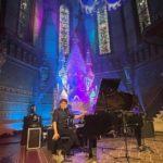 Portrait des Künstlers Lennert Schilgen vor dem Klavier in bunt beleuchteter Kirche
